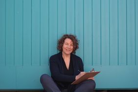 Kerstin sitzt vor einer blauen Mauer