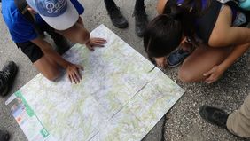 Mehrere Personen bücken sich über eine auf dem Boden ausgebreitete Wanderkarte