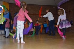 Mehrere Kinder und eine erwachsene Person tanzen in einem Raum und schwingen bunte Tücher