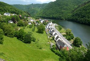 Landschaft mit einem Fluss, umgeben von grünen Hügeln und einem kleinen Dorf mit weißen und grauen Häusern.