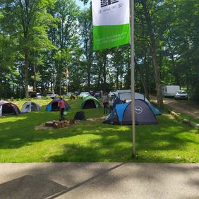 Ein Bild von einem Zeltplatz, der schön in einem Wald liegt. Die Zeltgruppe werden von der Sonne beschienen.