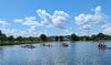 Das Bild zeigt einen See unter leicht bewöltem und sonnigem Himmel. Das Blau des Himmels spiegelt sich im See wieder. Auf dem See fahren Kanus. Die Leute lachen und haben viel Spaß.